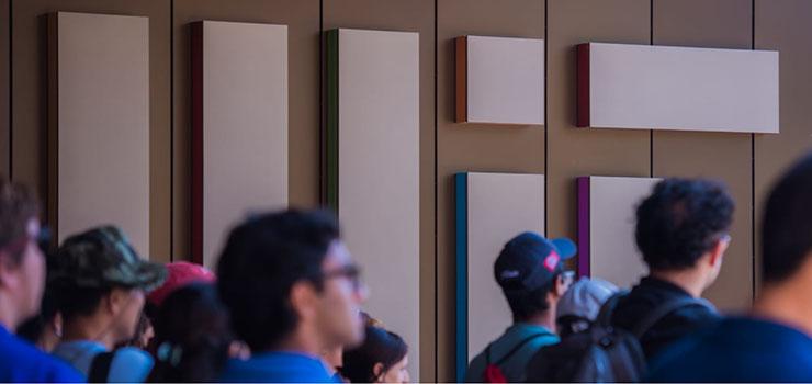 Visitors walk by a wall showing a large MIT logo